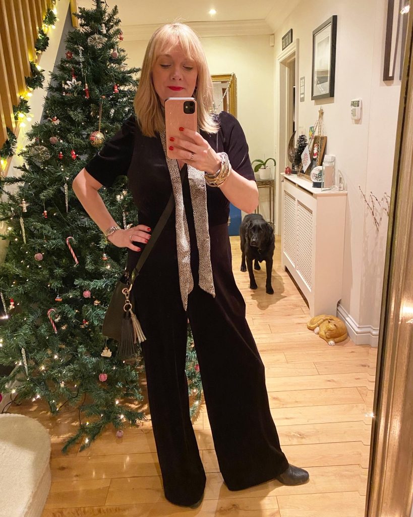 Mrs Stylewright wearing a velvet jumpsuit with a leopard print scarf in front of the Christmas tree