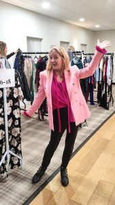 Michelle Wright dressed in pink showing off the rails of clothes at a Clothes Swap