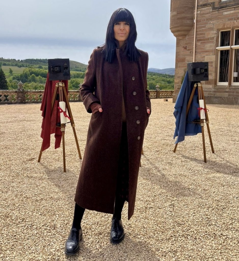 Claudia Winkleman outside the Traitors Castle wearing a long brown coat