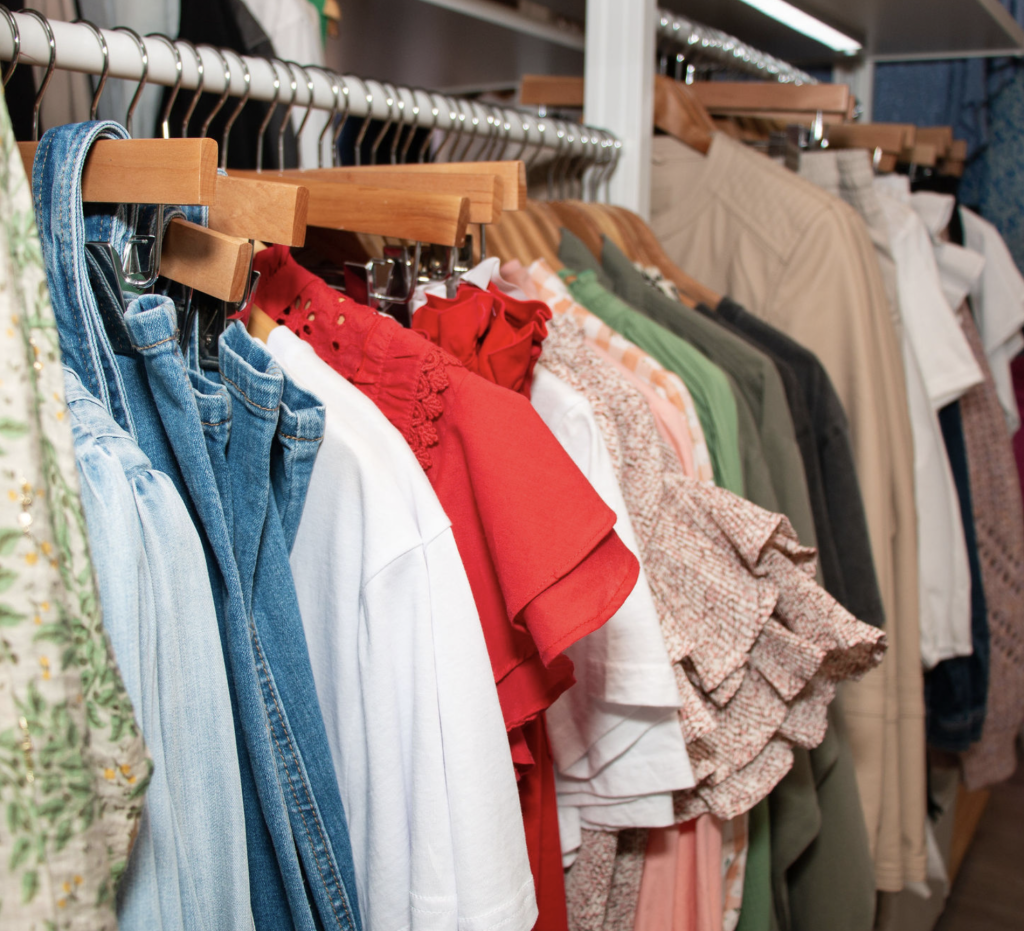 A rail of clothing hung on wooden hangers - some denim, cotton, jersey and knits in a variety of colours